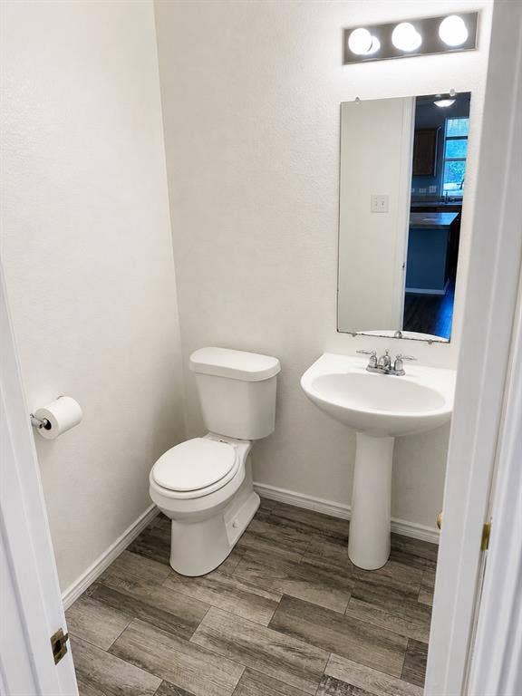 103 Denali Court, Terrell, TX 75160 Powder room featuring a pedestal sink, white toilet, wall-mounted mirror, and wood-finish flooring