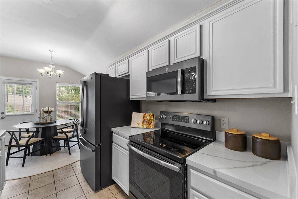 2408 Castle Ridge Drive, McKinney, TX 75071 Kitchen featuring stainless steel appliances, lofted ceiling, suspended lighting, light tile patterned flooring, and light stone counters