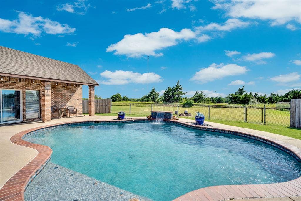 160 Berkshire Lane, Waxahachie, TX 75165 Backyard swimming pool with brick coping, concrete surround, and a waterfall feature