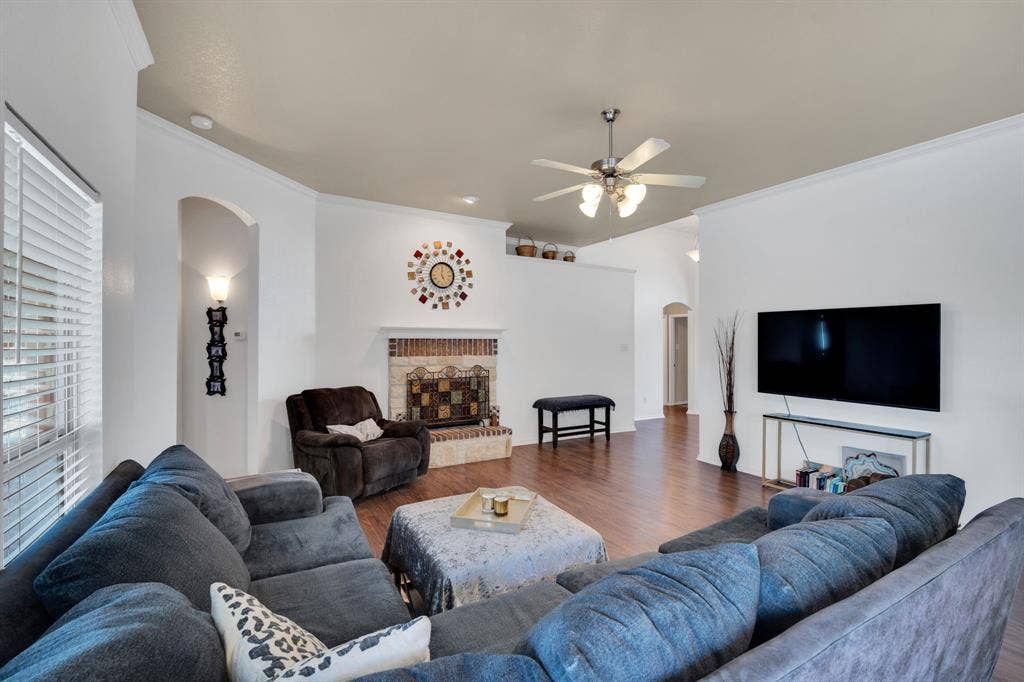 160 Berkshire Lane, Waxahachie, TX 75165 Living area featuring wood-finish flooring, a brick fireplace with a decorative tile surround, crown molding, and a ceiling fan