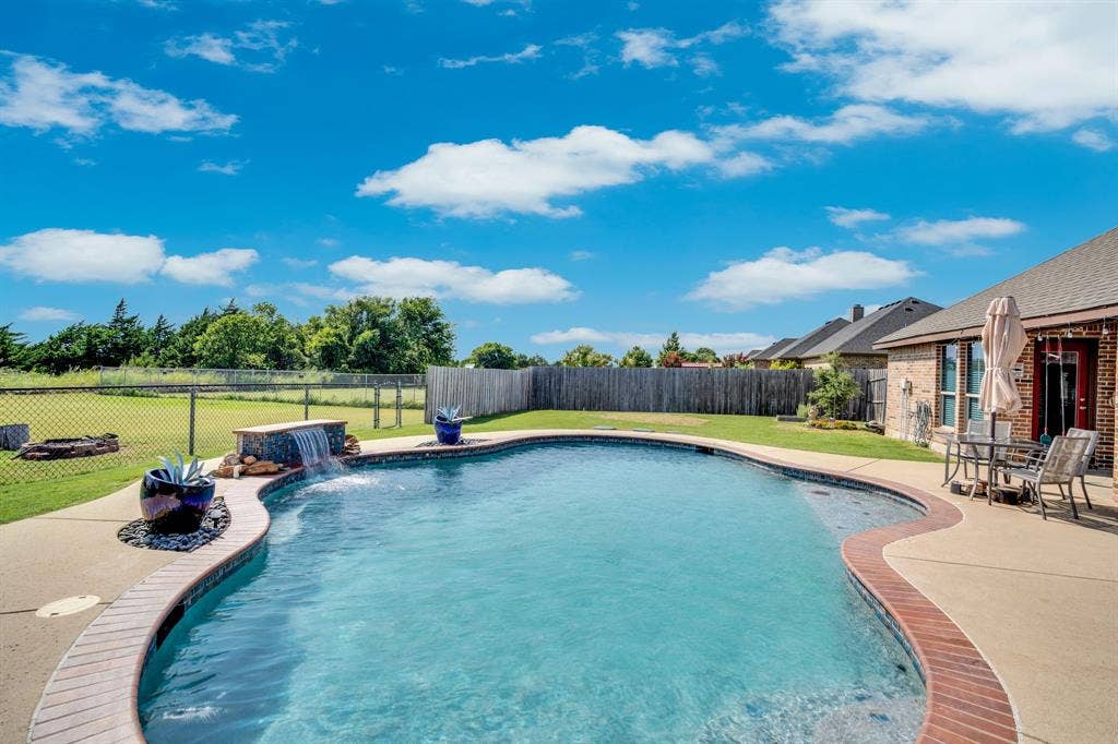 160 Berkshire Lane, Waxahachie, TX 75165 Curved swimming pool with a stone waterfall feature, brick coping, and integrated steps