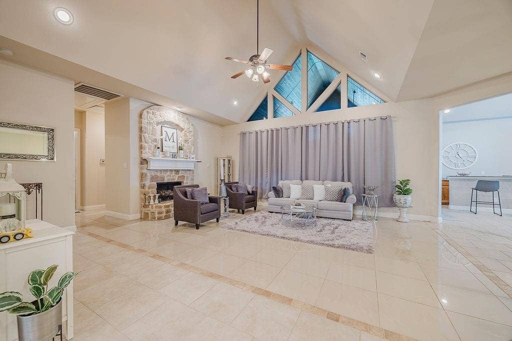 1011 Parview Circle, Grand Prairie, TX 75104 Living room with a high ceiling, inlaid floor details, a ceiling fan, light tile patterned floors, and a stone fireplace