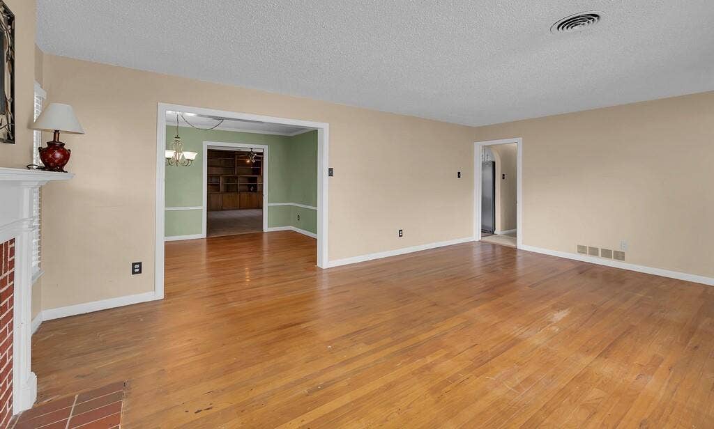3917 Morrow Avenue, Waco, TX 76710 Unfurnished living room featuring light wood-style floors, a brick fireplace, a textured ceiling, and suspended lighting
