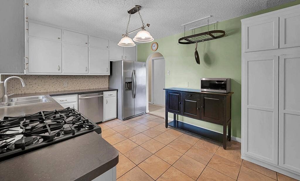 3917 Morrow Avenue, Waco, TX 76710 Kitchen featuring arched walkways, white cabinetry, stainless steel appliances, dark countertops, and a textured ceiling