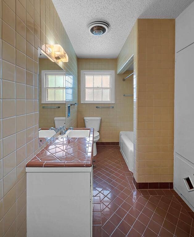 3917 Morrow Avenue, Waco, TX 76710 Bathroom featuring tile walls, a textured ceiling, dark tile patterned floors, vanity, and bathtub / shower combination