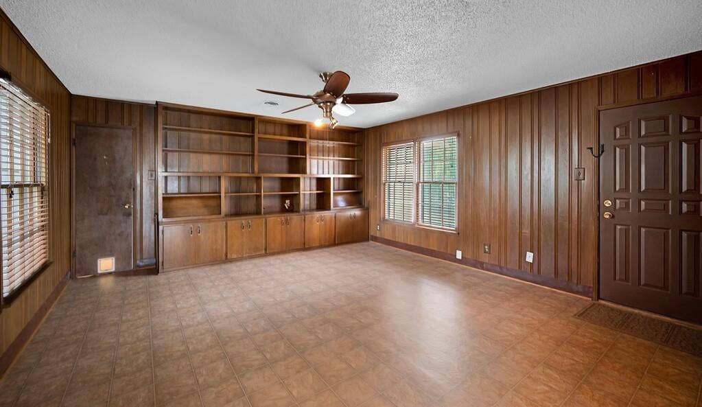 3917 Morrow Avenue, Waco, TX 76710 Unfurnished living room with wood walls, tile patterned floors, a ceiling fan, a textured ceiling, and built in features