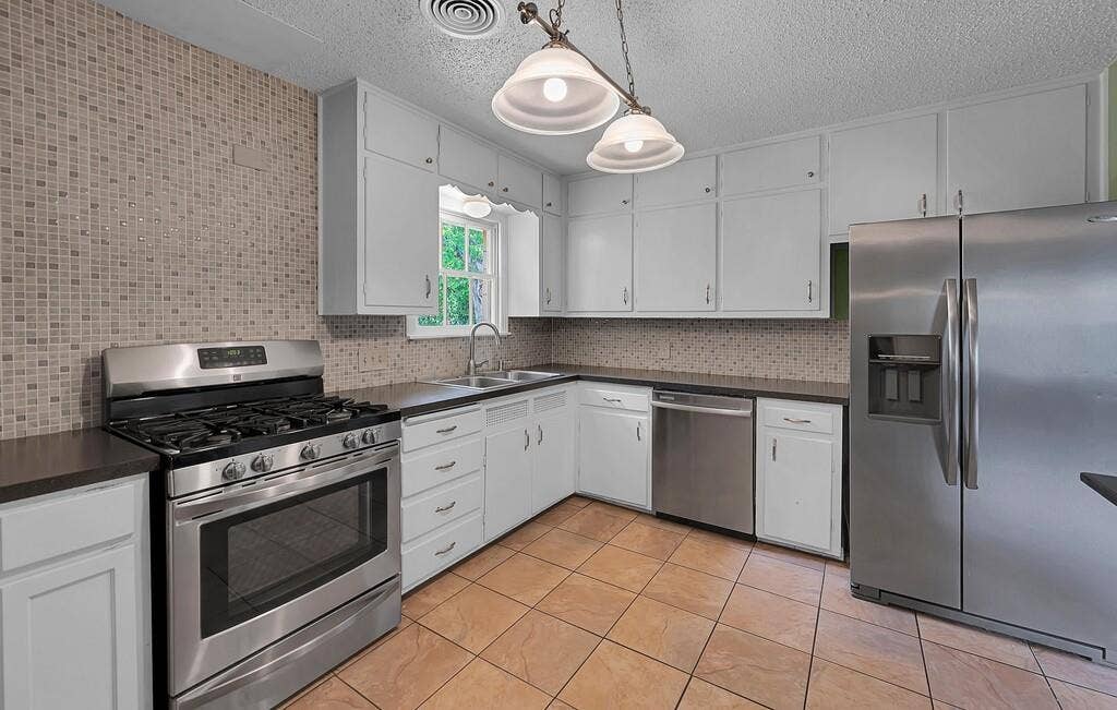 3917 Morrow Avenue, Waco, TX 76710 Kitchen featuring stainless steel appliances, dark countertops, white cabinets, hanging light fixtures, and tasteful backsplash