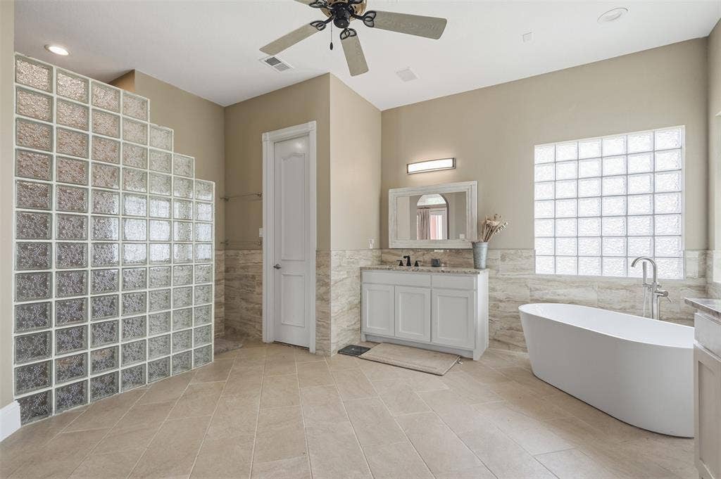 451 Land Of Goshen Drive, Springtown, TX 76082 Spacious bath featuring a freestanding soaking tub, single vanity with light-toned countertop, floor-to-ceiling glass block shower enclosure, and large format tile flooring
