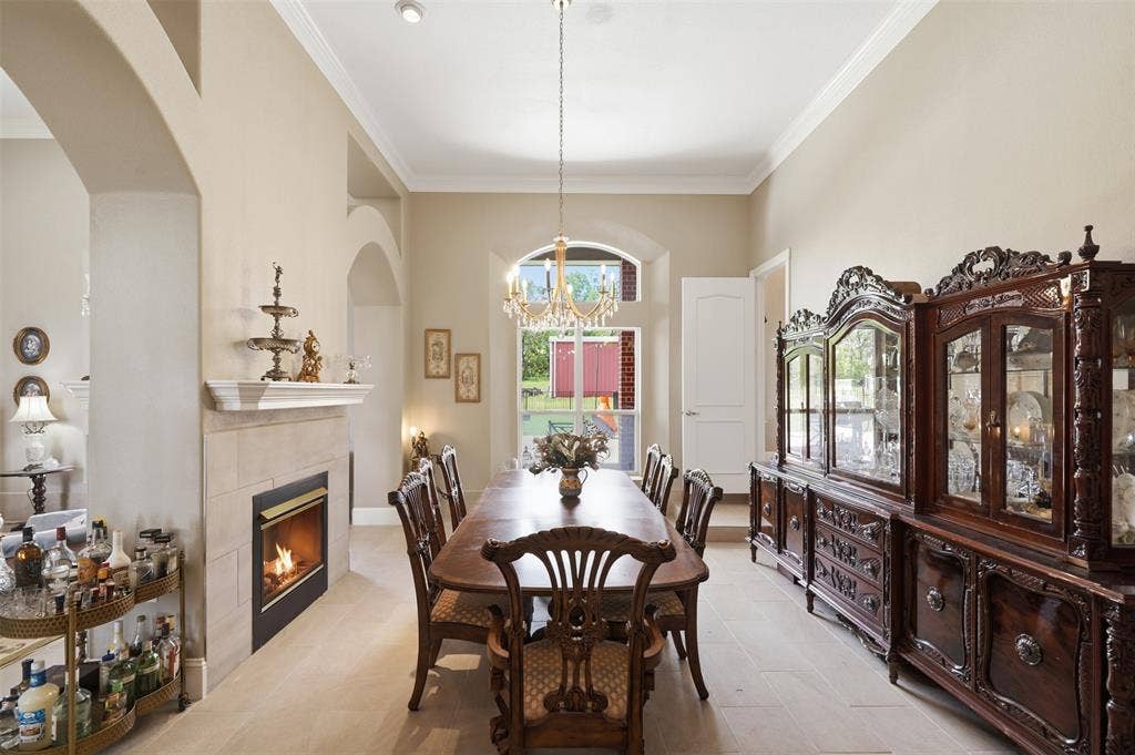 451 Land Of Goshen Drive, Springtown, TX 76082 Spacious dining area featuring a fireplace with a light-toned tile surround and mantel, arched architectural details, recessed lighting, crown molding, and a chandelier