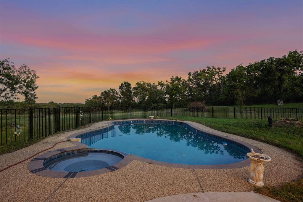 451 Land Of Goshen Drive, Springtown, TX 76082 Kidney-shaped swimming pool featuring a built-in spa, aggregate concrete decking, and a black wrought-iron fence