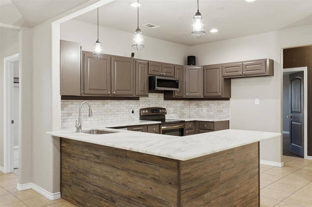 113 Mulkey Road, Waxahachie, TX 75167 Kitchen with light tile patterned floors, a peninsula, hanging light fixtures, stainless steel appliances, and decorative backsplash