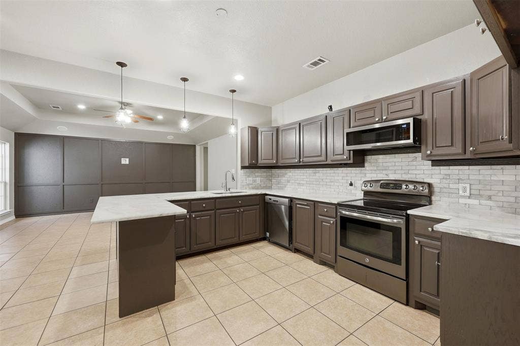 113 Mulkey Road, Waxahachie, TX 75167 Kitchen with a tray ceiling, stainless steel appliances, a peninsula, pendant lighting, and a ceiling fan