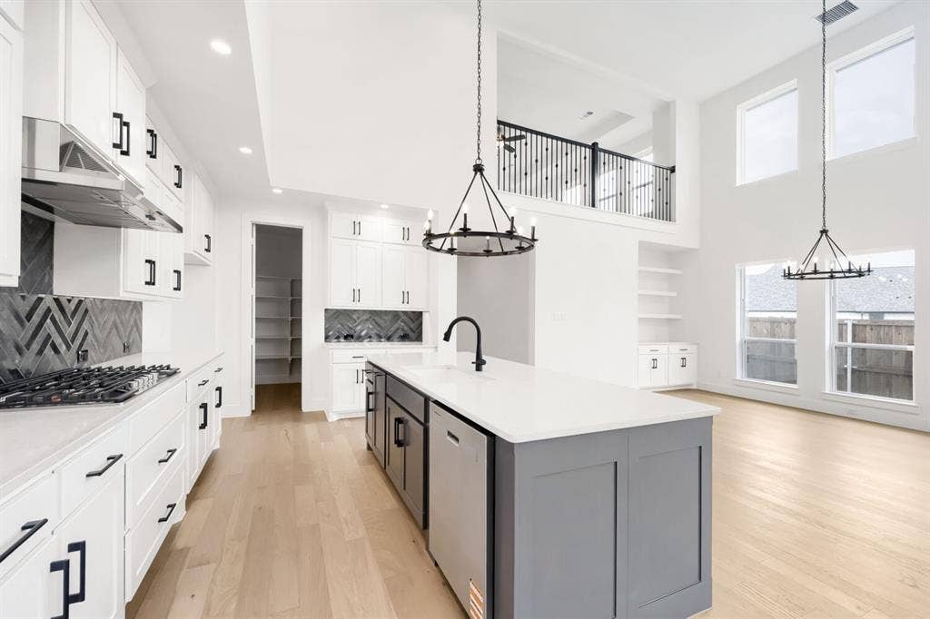 733 Red Cedar Road, Haslet, TX 76052 Modern kitchen featuring white cabinetry, black hardware, stainless steel appliances, a gray island with a white countertop, and herringbone tile backsplashes