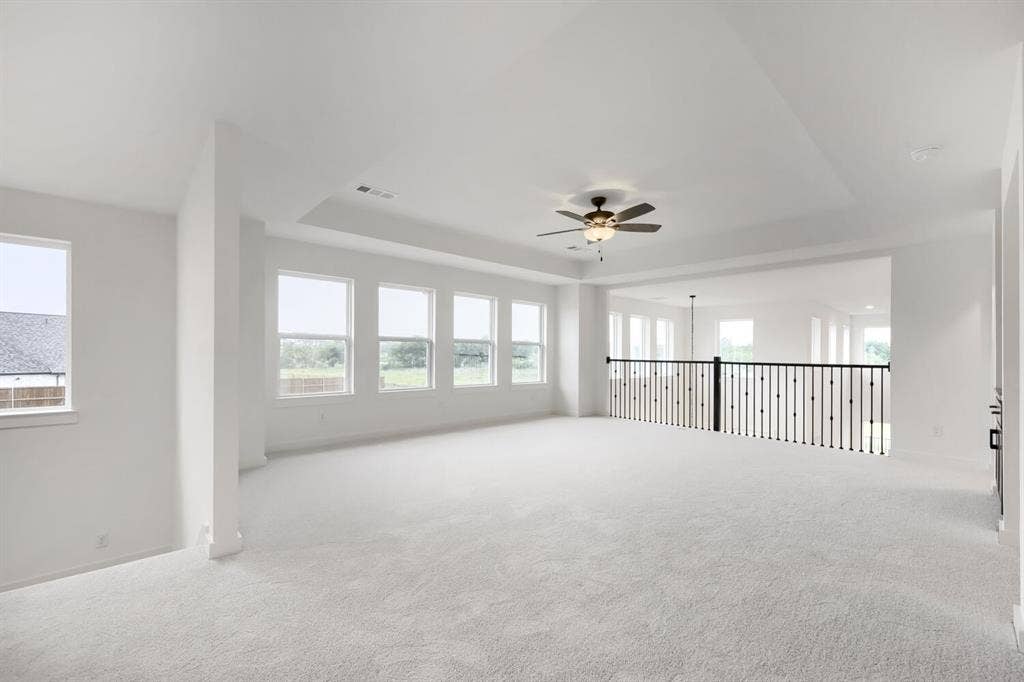 733 Red Cedar Road, Haslet, TX 76052 Spacious loft area featuring light carpet flooring, a multi-window wall, and a tray ceiling with a ceiling fan