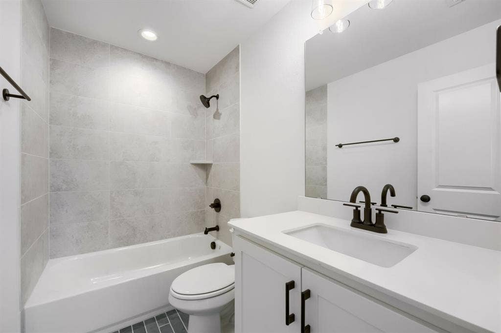 733 Red Cedar Road, Haslet, TX 76052 Bathroom featuring a white bathtub with light gray tile surround, dark bronze fixtures, white vanity with integrated sink, and a large mirror