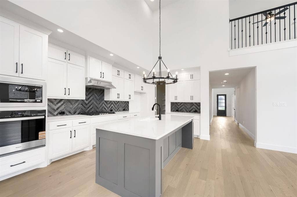 733 Red Cedar Road, Haslet, TX 76052 Contemporary kitchen featuring white cabinetry with black hardware, a herringbone pattern tile backsplash, and a central island with a light-toned countertop