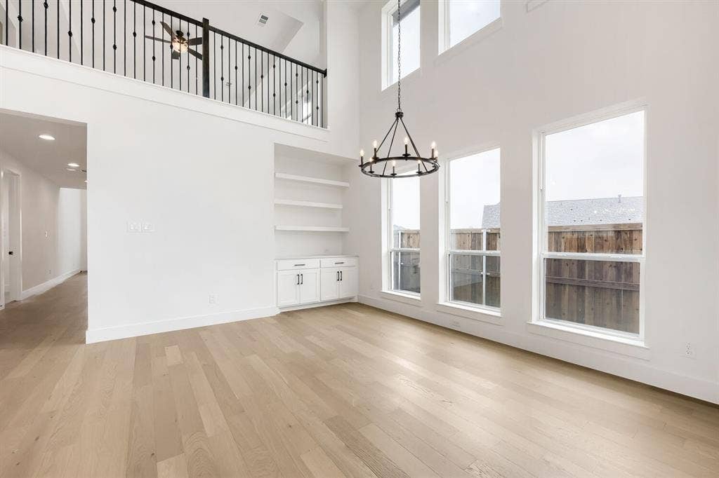 733 Red Cedar Road, Haslet, TX 76052 Spacious room featuring soaring ceilings, abundant natural light from multiple windows, wood-finish flooring, built-in shelving, and a decorative chandelier