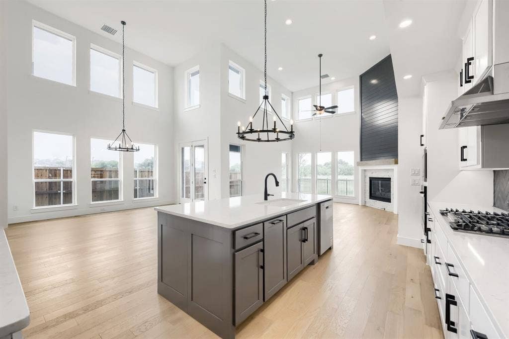 733 Red Cedar Road, Haslet, TX 76052 Open-concept living area featuring a kitchen island with stone countertop, wood-finish flooring, a contemporary fireplace with a shiplap accent wall, high ceilings, and abundant natural light from numerous windows