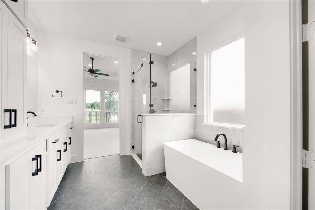 733 Red Cedar Road, Haslet, TX 76052 Spacious bathroom featuring a freestanding soaking tub with matte black fixtures, a walk-in shower with glass enclosure, dual vanity with white cabinetry and dark hardware, and dark tile flooring