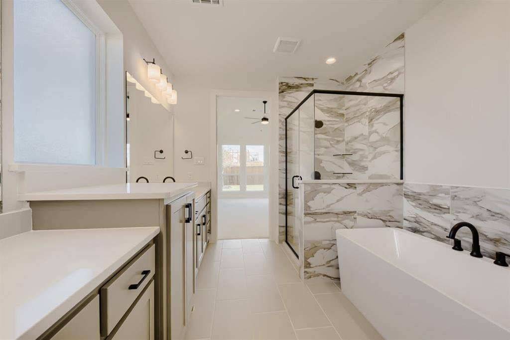 1241 Greenbriar Avenue, Haslet, TX 76052 Bathroom featuring a freestanding soaking tub with matte black fixtures, a glass-enclosed shower with contrasting tile, and dual vanity areas with white countertops and undermount sinks