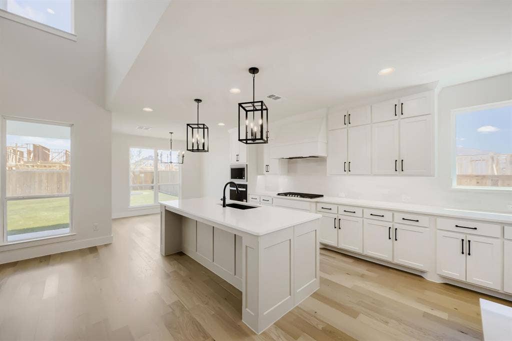 1241 Greenbriar Avenue, Haslet, TX 76052 Open-concept kitchen featuring an island with built-in sink, white cabinetry with black hardware, recessed lighting, and wood-finish flooring