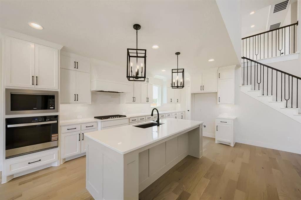 1241 Greenbriar Avenue, Haslet, TX 76052 Gourmet kitchen featuring white shaker cabinetry, an expansive center island with an undermount sink and matte black faucet, stainless steel built-in appliances, and light wood-finish flooring