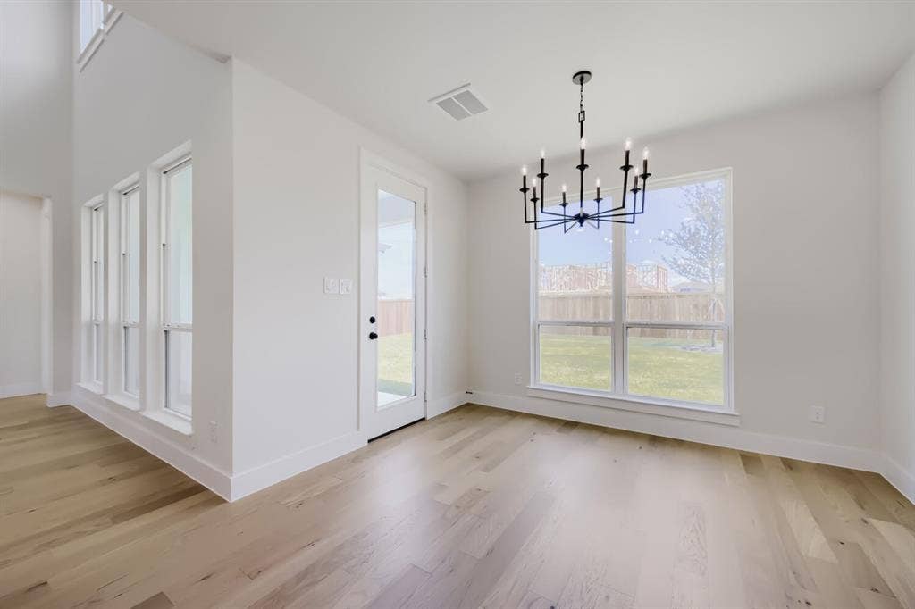 1241 Greenbriar Avenue, Haslet, TX 76052 Spacious room featuring light wood-finish flooring, a modern black chandelier, multiple large windows, a full-lite glass door, and high ceilings