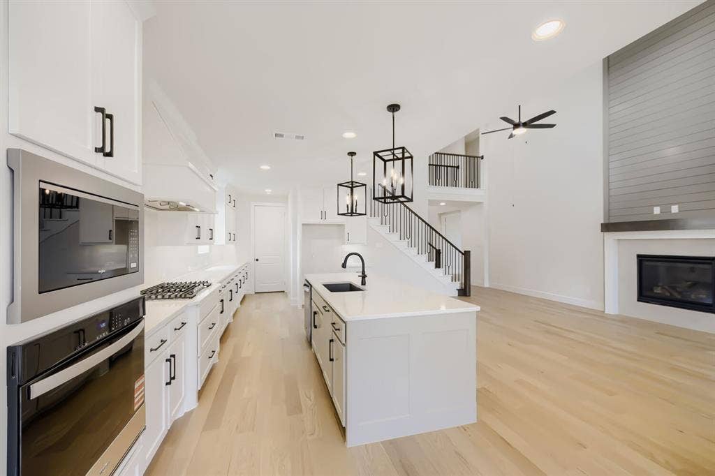 1241 Greenbriar Avenue, Haslet, TX 76052 Open concept living space featuring a modern kitchen with white cabinetry and a central island, light wood-finish flooring, a contemporary fireplace with shiplap accent wall, and an open staircase with wrought iron balusters