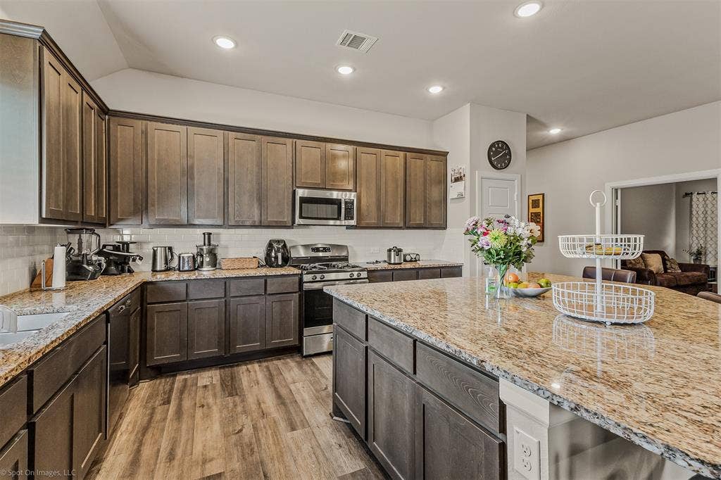 5408 Wedge Wood Drive, Haltom City, TX 76137 Kitchen featuring stainless steel appliances, light wood-style floors, light granite countertops, recessed lighting, and dark wood finish cabinets