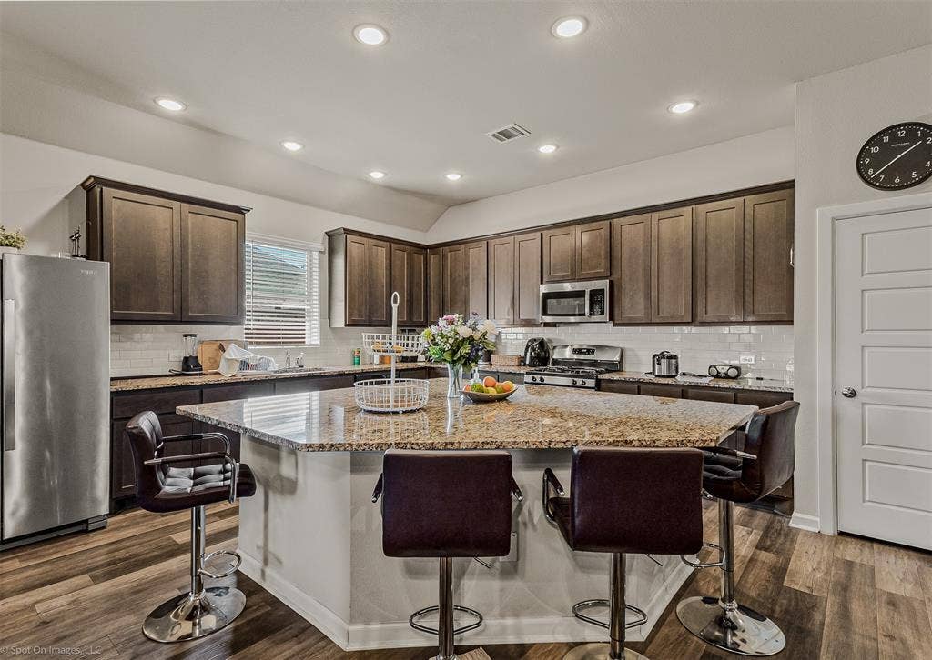 5408 Wedge Wood Drive, Haltom City, TX 76137 Kitchen featuring stainless steel appliances, a kitchen breakfast bar, dark wood finish cabinets, light stone counters, and a kitchen island