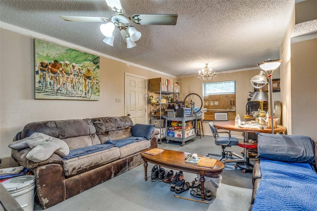 Living room with concrete floors, a textured ceiling, a chandelier, a ceiling fan, and crown molding