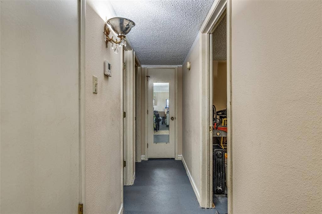 Hallway featuring finished concrete flooring, a textured ceiling, and a textured wall