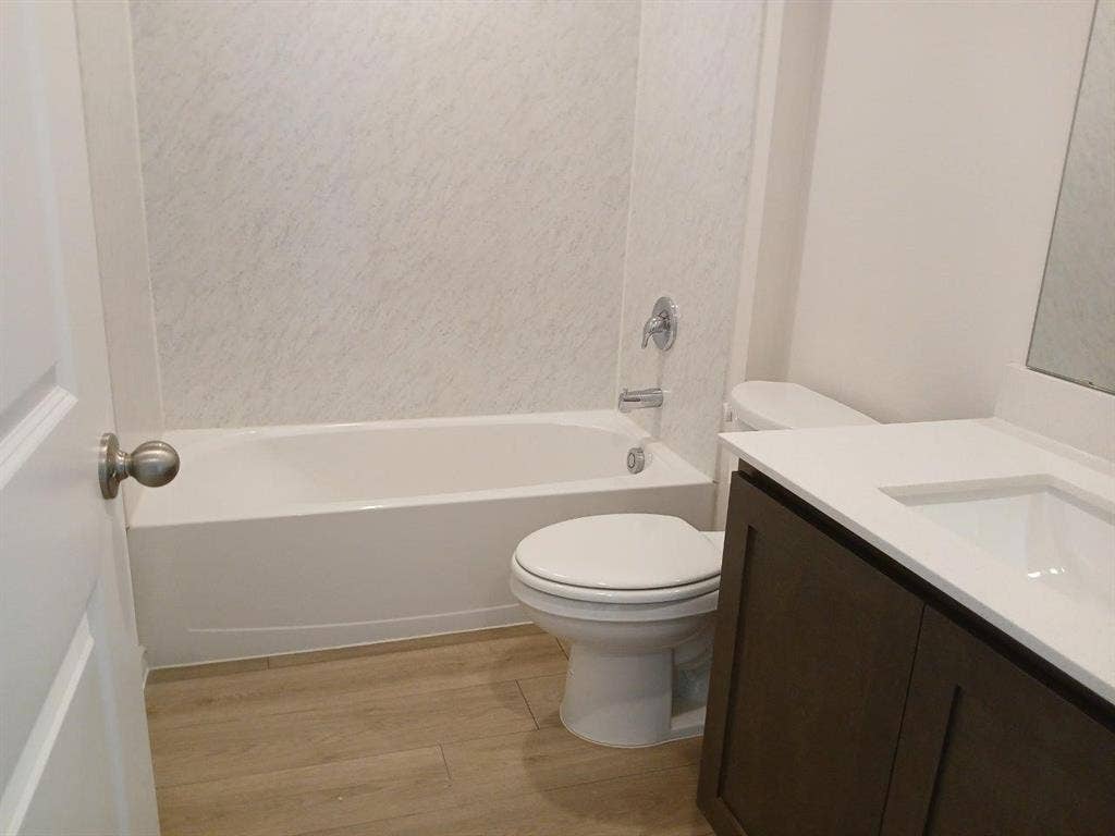 315 Whispering Pine Drive, Royse City, TX 75189 Full bathroom featuring a white tub with integrated shower, white toilet, wood-finish flooring, a dark wood-finish vanity, and a white countertop with an integrated sink