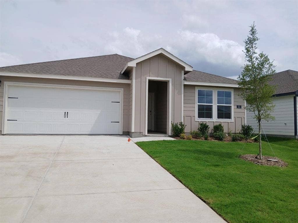 315 Whispering Pine Drive, Royse City, TX 75189 Single-story residence featuring a two-car garage with decorative hardware, a light brown facade, and a dark shingle roof