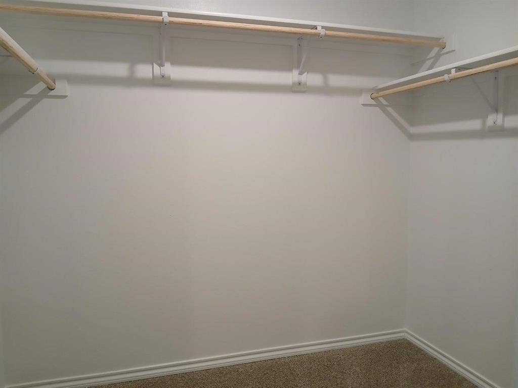 315 Whispering Pine Drive, Royse City, TX 75189 Spacious closet featuring multiple wood closet rods on white shelving brackets, light-colored carpeting, and white baseboard trim