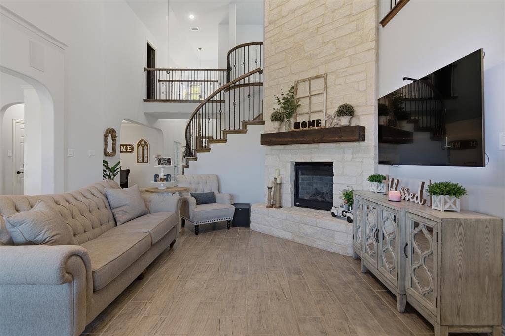 Two-story living area featuring wood-finish flooring, a stone-clad fireplace with a dark wood mantel, and a prominent curved staircase with dark wood handrails and black metal balusters
