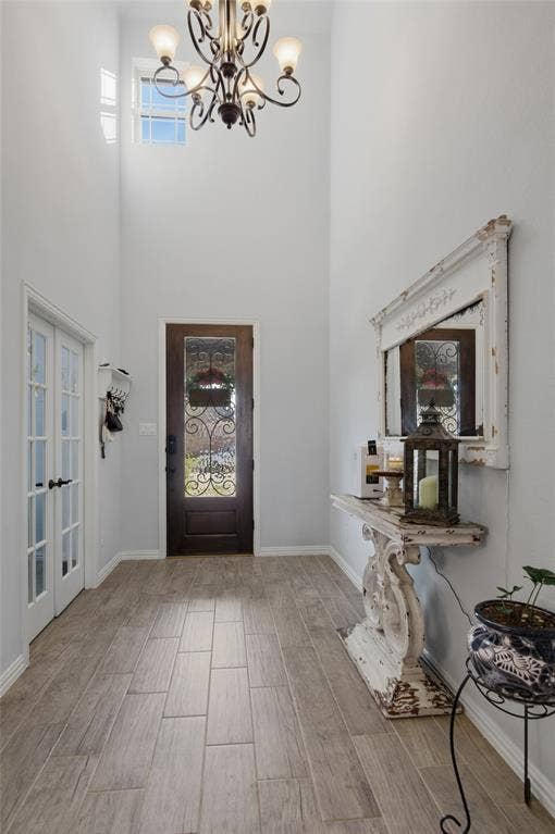 Two-story foyer featuring a decorative chandelier, a transom window, a dark wood-finish front door with an ornate glass insert, wood-finish tile flooring, and white trim throughout