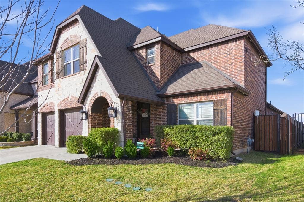 Two-story brick and stone exterior featuring an arched entry, two-car garage, and dark wood shutters