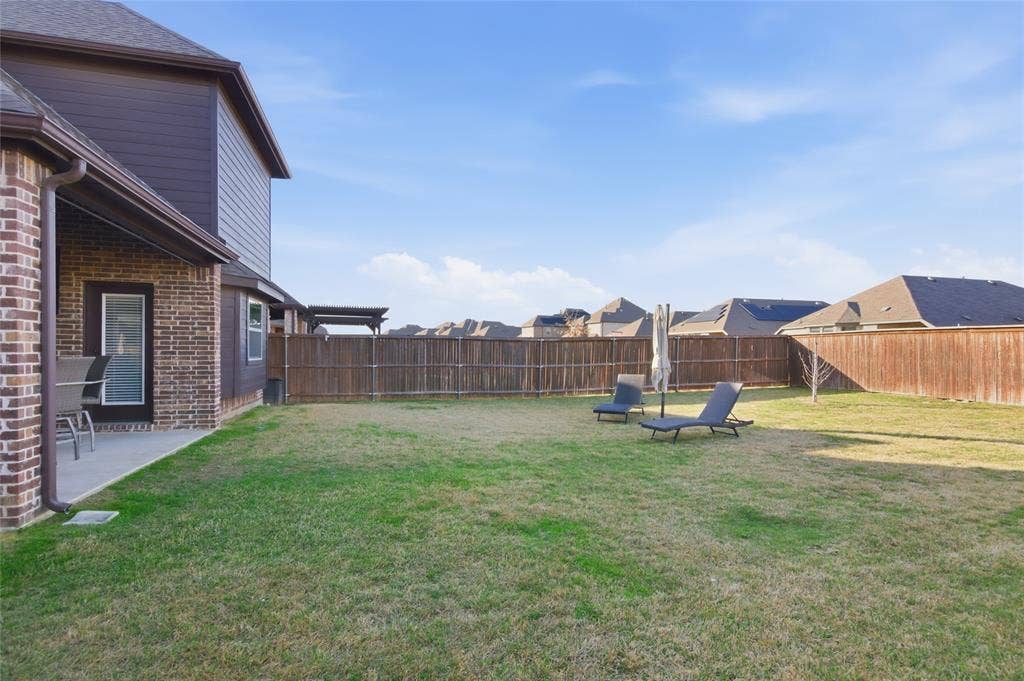 Expansive backyard featuring a manicured lawn, full privacy fencing, and a concrete patio