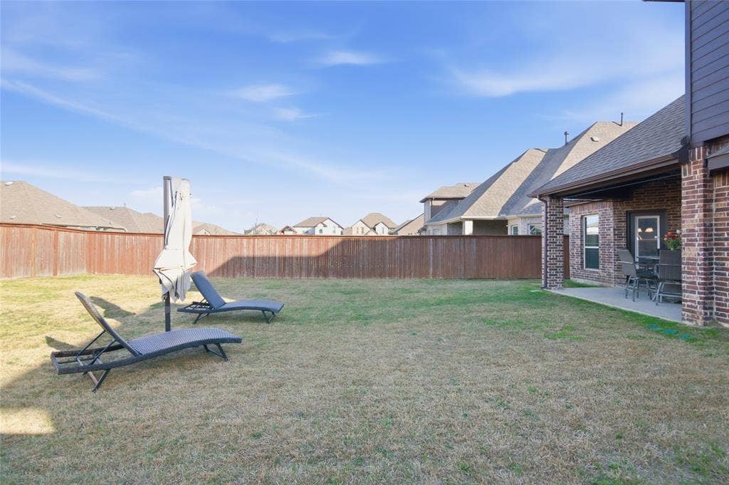 Spacious backyard featuring a manicured lawn, full privacy fencing, and an attached covered patio