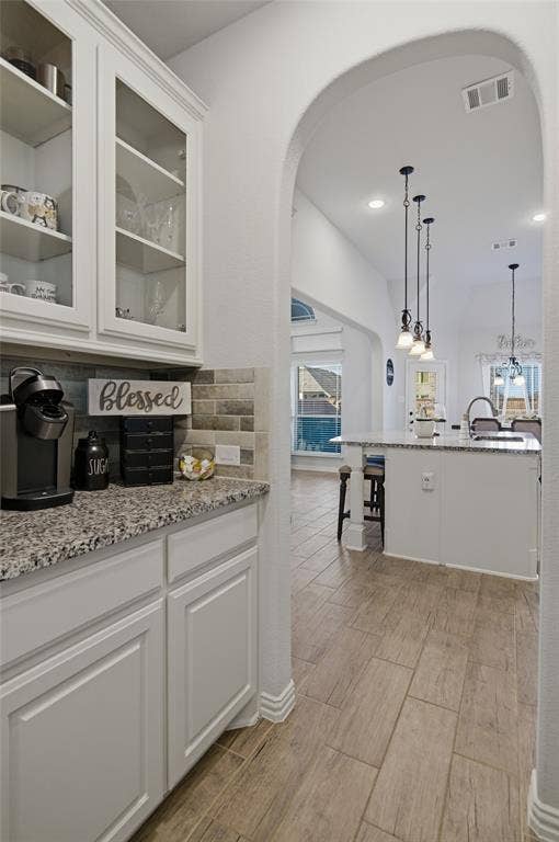 Kitchenette area with white shaker-style cabinetry, glass-front upper cabinets, and a speckled countertop