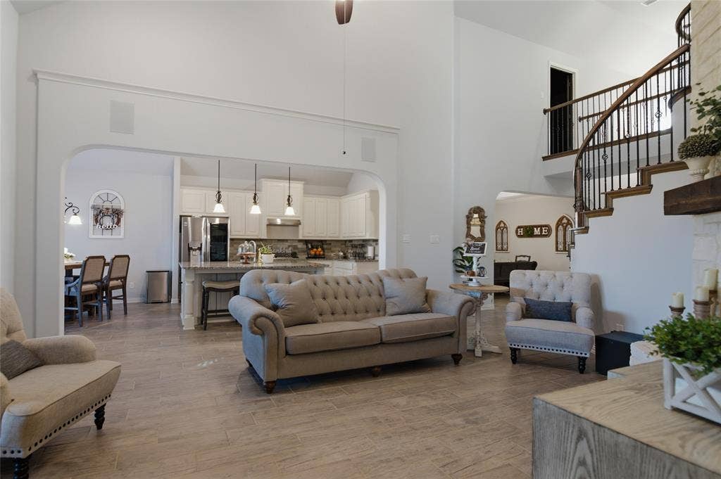 Spacious living area featuring wood-finish flooring, a soaring two-story ceiling, and an elegant curved staircase with wrought iron balusters