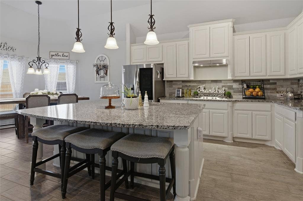 Kitchen featuring a spacious island with a granite countertop, white paneled cabinetry, stainless steel appliances, a tiled backsplash, and wood-finish flooring
