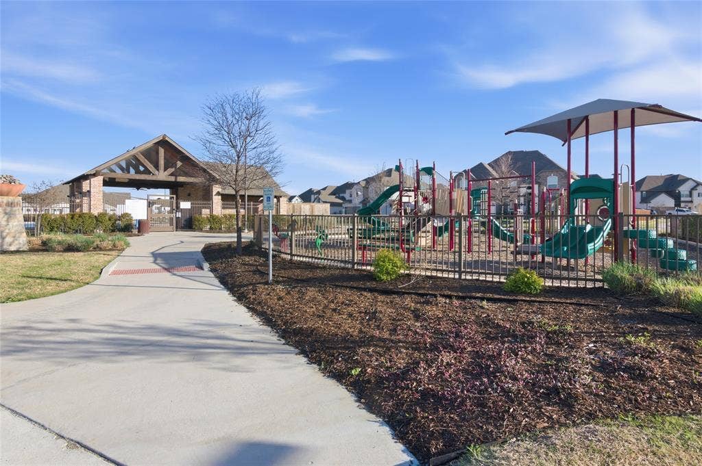 Community playground featuring multiple slides, climbing structures, and protective surfacing, enclosed by a metal fence