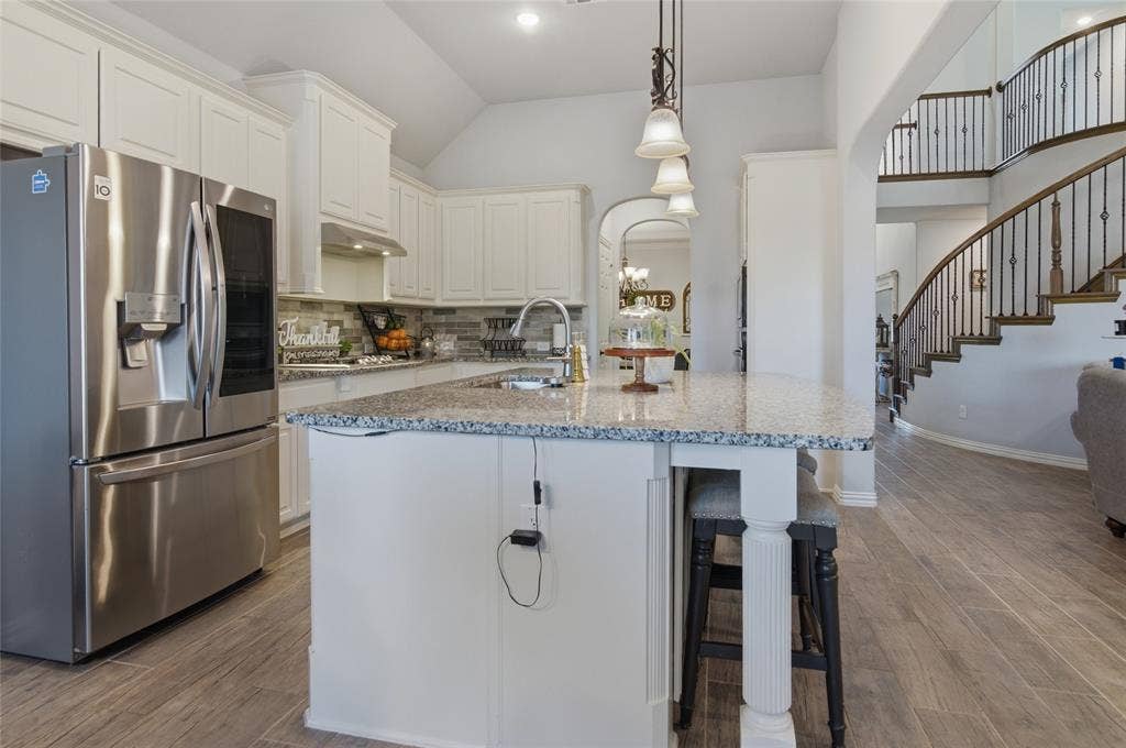 Gourmet kitchen with white cabinetry, stainless steel appliances, a large island with integrated seating, and wood-finish flooring