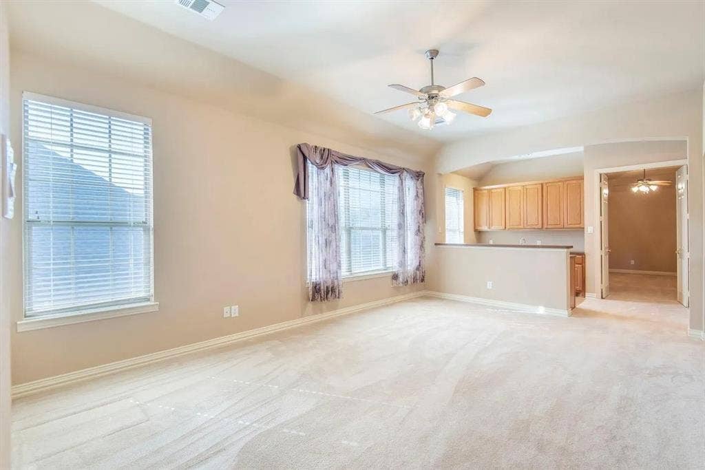 15031 Woodbluff Drive, Frisco, TX 75035 Open-concept living area featuring light-toned carpeting, multiple windows with blinds, a ceiling fan with integrated lighting, and a breakfast bar with built-in cabinetry