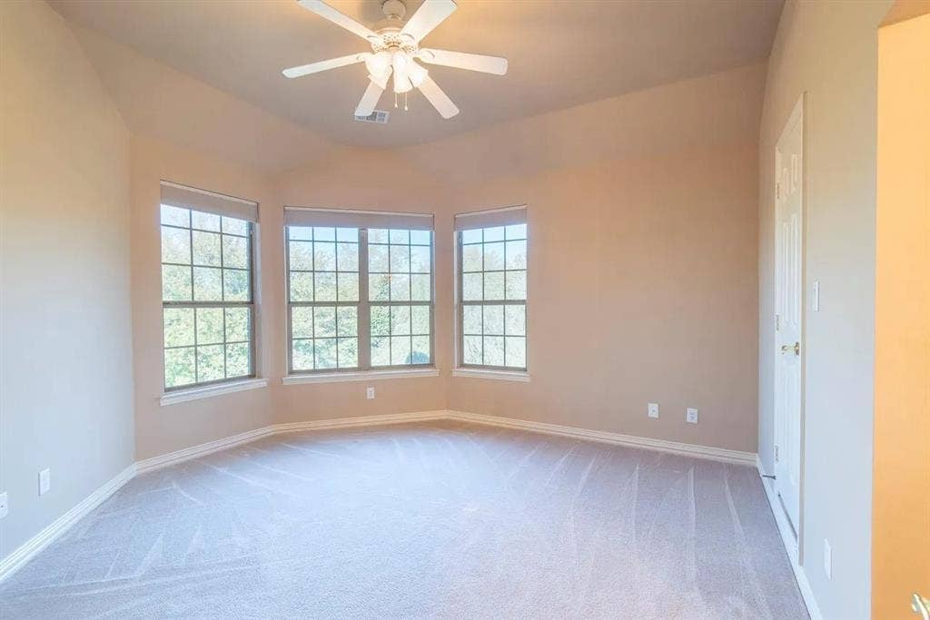 15031 Woodbluff Drive, Frisco, TX 75035 Spacious room featuring a bay window with three large windows, a vaulted ceiling, a ceiling fan, plush carpeting, and neutral paint tones