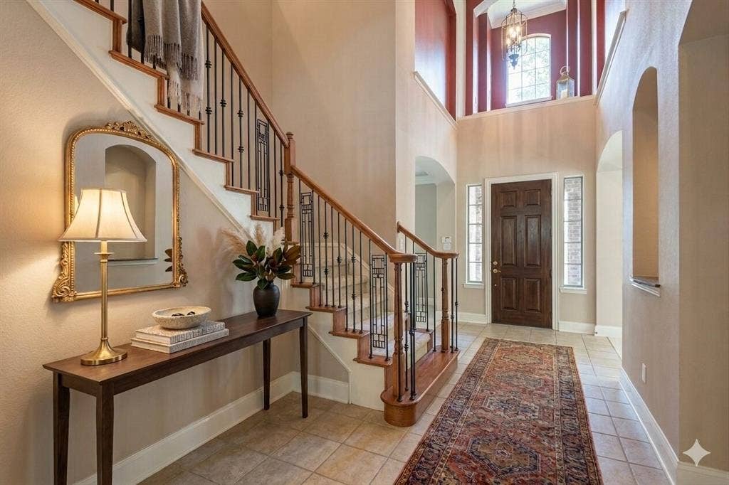 15031 Woodbluff Drive, Frisco, TX 75035 Gracious foyer featuring a dark wood front door with sidelight windows, tile flooring, and a grand staircase with wood handrails and wrought iron balusters