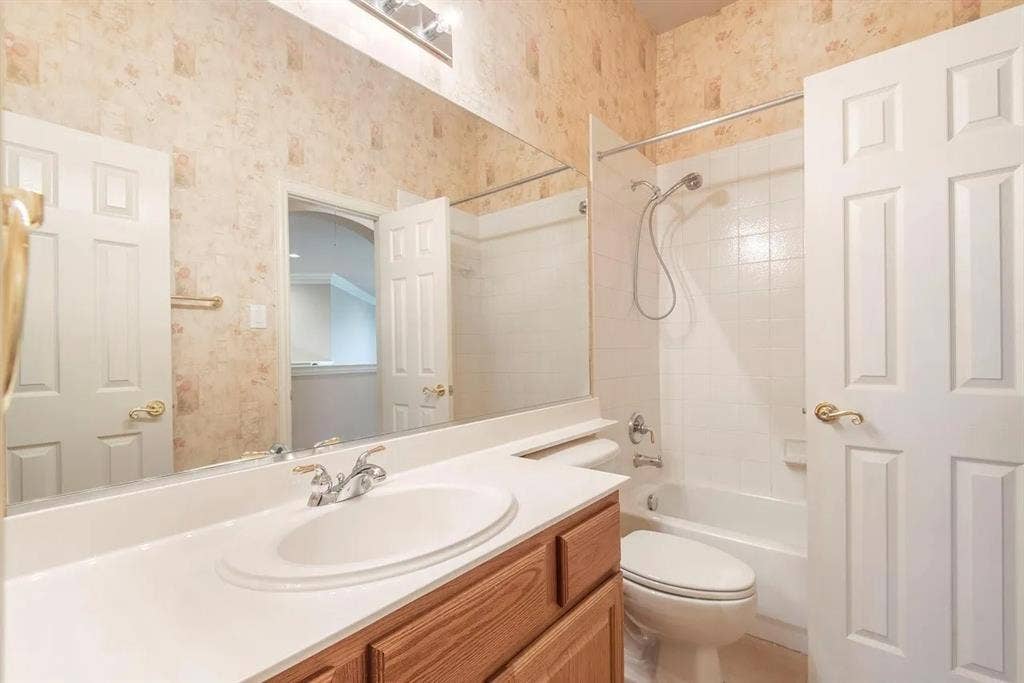 15031 Woodbluff Drive, Frisco, TX 75035 Full bathroom featuring a single-sink vanity with a white countertop and wood-finish cabinetry, a built-in tub with white tile surround, and two panel doors