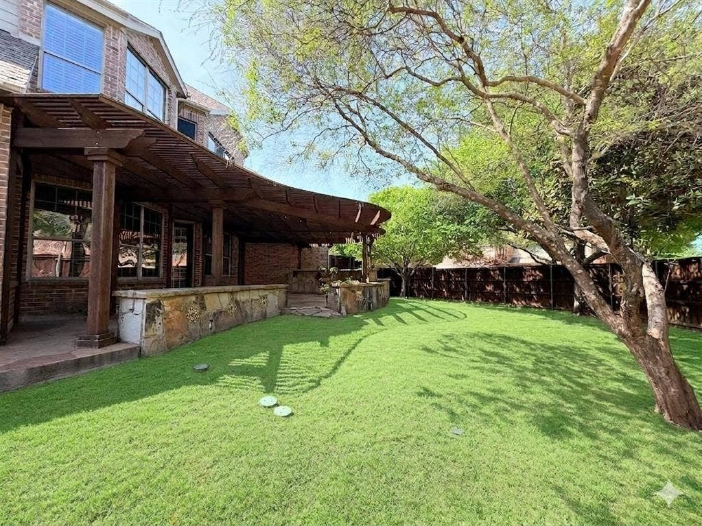 15031 Woodbluff Drive, Frisco, TX 75035 Spacious backyard featuring a manicured lawn, established shade trees, and a wooden pergola covering a stone patio